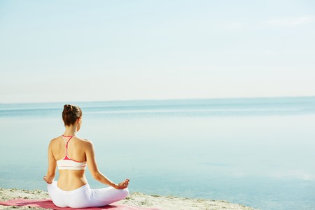 Meditating woman sitting on sandy beachの写真素材