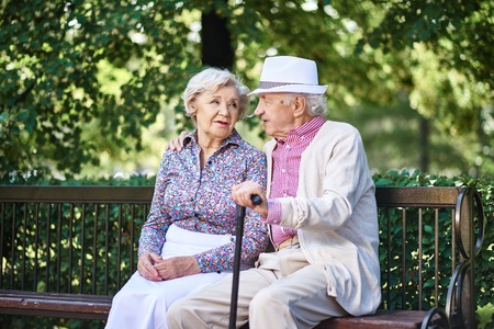 Senior couple in smart casual sitting on bench in park and interactingの写真素材