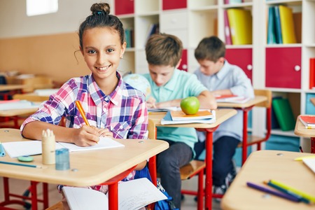 Pretty schoolgirl sitting at lesson with open copybook on her kneesの写真素材