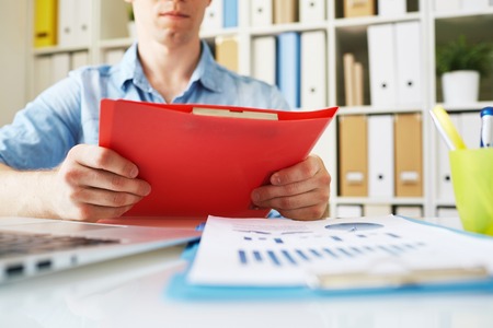 Businessman holding red folder over workplaceの写真素材
