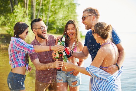 Ecstatic friends toasting with beer in water splashesの写真素材