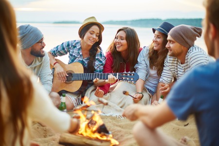 Friendly girls and guys singing by guitar by campfire