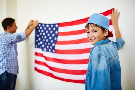 Handsome boy looking at camera while holding USA flag hanging on wallの写真素材