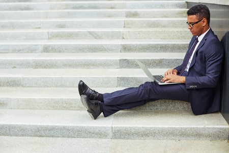 Young businessman using laptop while sitting on stairsの写真素材