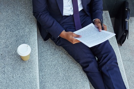 Close-up of businessman reading document on stairsの写真素材