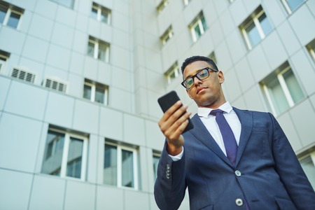 Serious businessman reading sms on background of modern buildingの写真素材