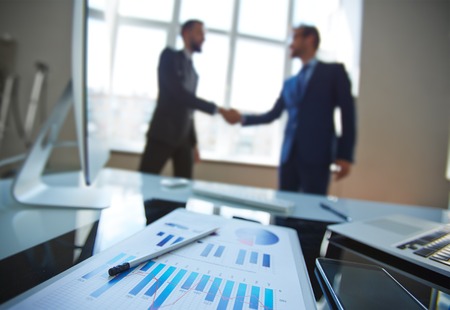 Business document at workplace with business partners handshaking on background