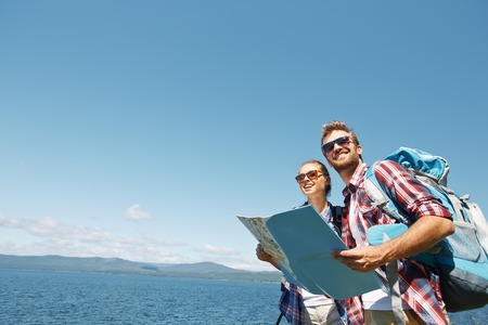 Cheerful hikers with map enjoying their trip on background of sky and seaの写真素材