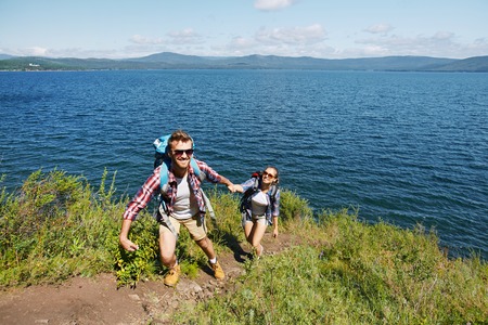 Happy young traveler helping his girlfriend to climb on mountの写真素材