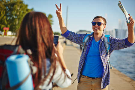 Modern woman with cellphone taking photo of her boyfriend outdoors