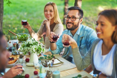 Happy Asian man with glass of red wine sitting at Thanksgiving partyの写真素材