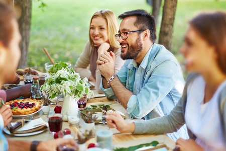 Happy Asian man in eyeglasses and casualwear sitting by Thanksgiving tableの写真素材