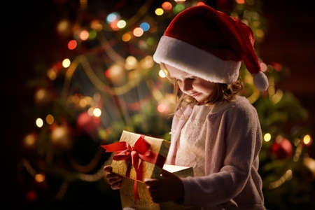 Adorable girl in Santa cap opening magic giftbox on xmas nightの写真素材