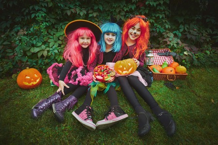 Happy girls in wigs and Halloween costumes holding pumpkins and sweetsの写真素材