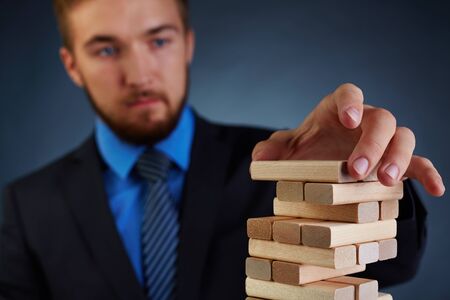 Businessman putting small wooden block on top of towerの写真素材