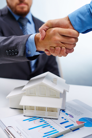 Buyer and vendor of real estate handshaking over model of houseの写真素材