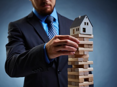 Businessman touching wooden tower with house on its topの写真素材