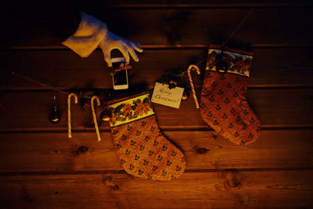 Christmas socks, sugar canes, toy bubbles on wooden background and cellphone bound with ribbon in gloved Santa handの写真素材