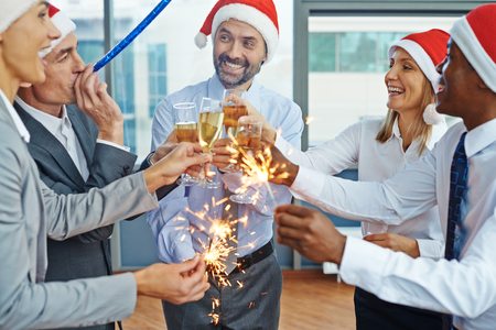 Happy colleagues in Santa caps having Christmas fun while toasting with champagne at party in officeの写真素材