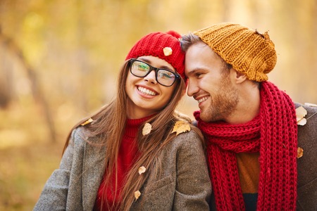 Happy young couple looking at camera during leaf fallの写真素材