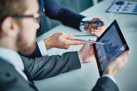 Businessman holding touchpad with data being explained by his colleague