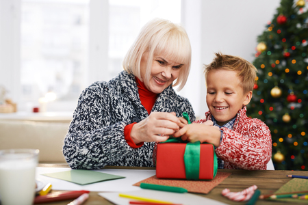 Mature woman helping her grandson tie package with giftの写真素材