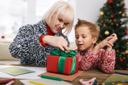 Mature woman helping her grandson tie gift-boxの写真素材