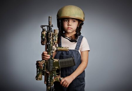 Little girl with gun wearing protective helmetの写真素材