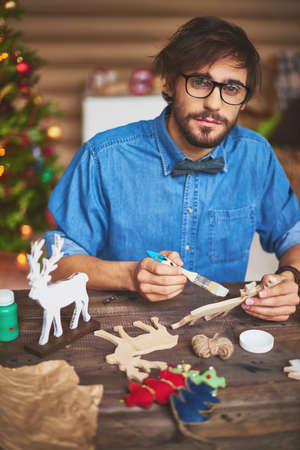 Young man painting Christmas symbols with gouache and looking at cameraの写真素材