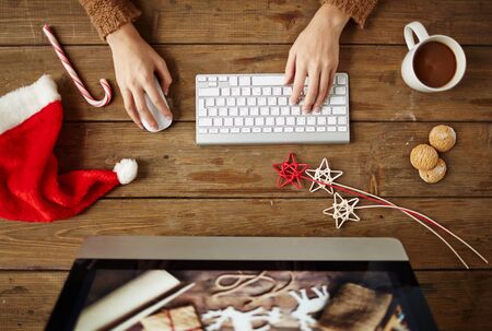 Woman typing at workplace with coffee, biscuits and Christmas symbols near byの写真素材
