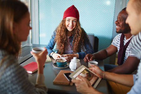 Young female in knitted cap and her friends spending time in cafeの写真素材