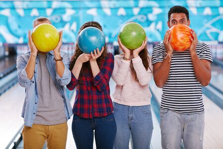 Teenagers hiding their faces behind bowling ballsの写真素材