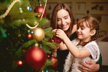 Cute girl and her mother decorating firtree on Christmas eveの写真素材