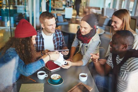 Happy young friends spending leisure by talking in cafeの写真素材