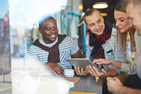 Group of young friends with touchpad networking in cafe