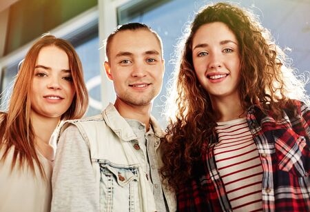 Three young friends in casual-wear looking at cameraの写真素材