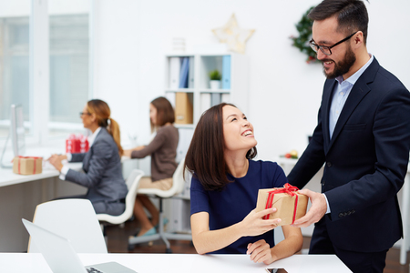 Handsome businessman making Christmas surprise to his secretary in officeの写真素材