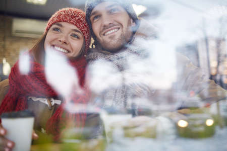 Smiling couple in winter-wear having drink in cafe