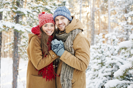 Embracing couple looking at camera with smiles in winter parkの写真素材