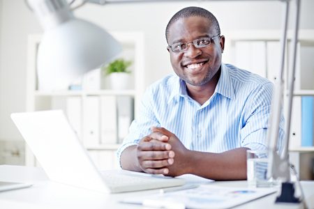 Smiling businessman sitting at his table at officeの写真素材