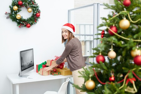 Santa businesswoman preparing Christmas presents for colleagues in officeの写真素材