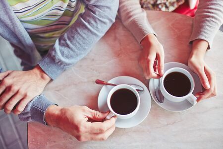 Close up of table and hands of young couple enjoying a cup of coffee at sidewalk restaurantの写真素材