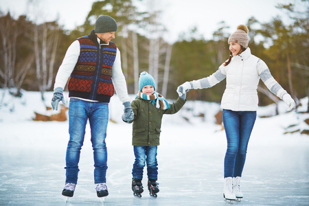 Young family holding hands and ice skating on rinkの写真素材