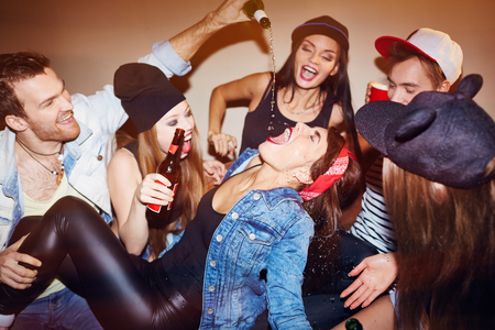 Ecstatic friends pouring beer into girl mouth at swag partyの写真素材