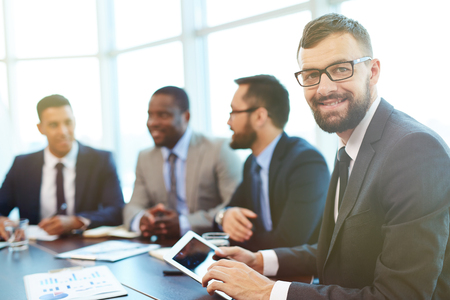 Happy businessman with touchpad looking at camera in working environmentの写真素材
