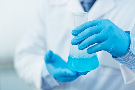 Modern scientist in protective gloves holding tube with blue fluidの写真素材