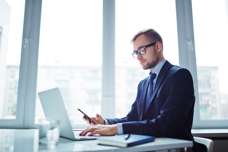 Confident businessman using modern gadgets in officeの写真素材