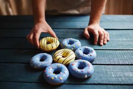 Baker putting doughnuts with icing on wooden tableの写真素材