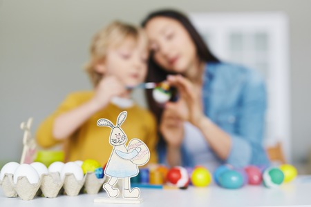 Paper rabbit with egg on background of painting woman and boy
