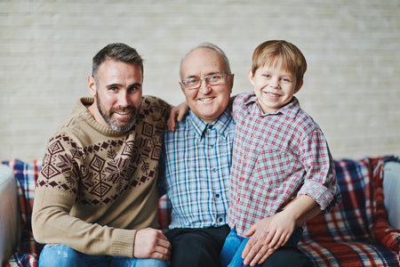 Happy mature man, young man and little boy sitting on sofaの写真素材